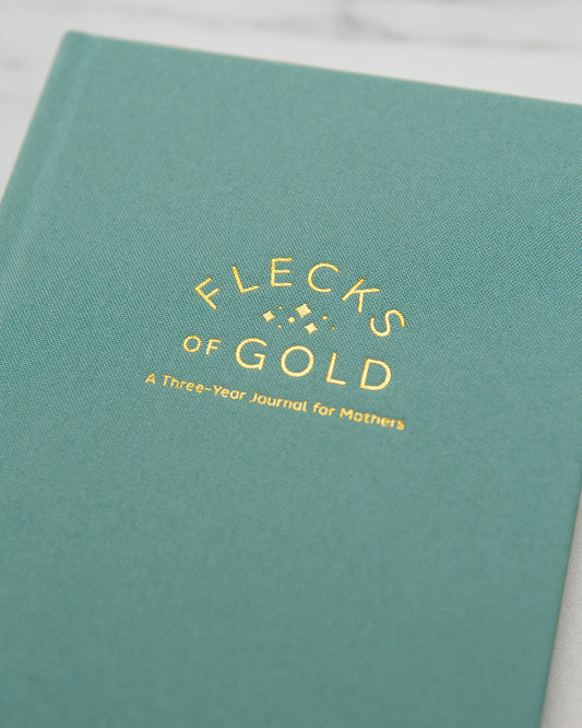 Close-up of the gold-foil embossed title on the teal linen cover: Flecks of Gold, A Three-Year Journal for Mothers