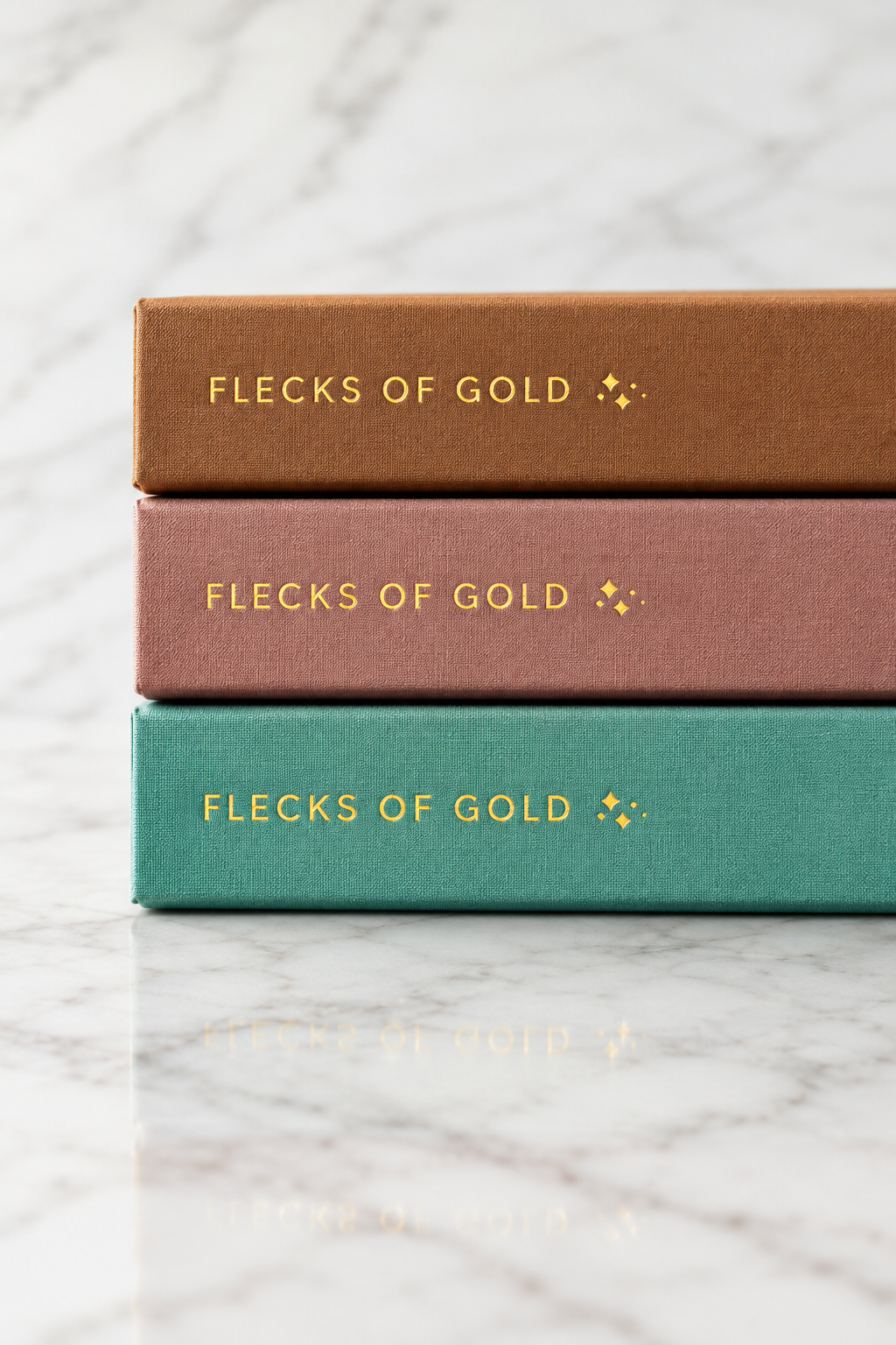 Gold-foil Flecks of Gold spines on stacked camel, rose and teal journals