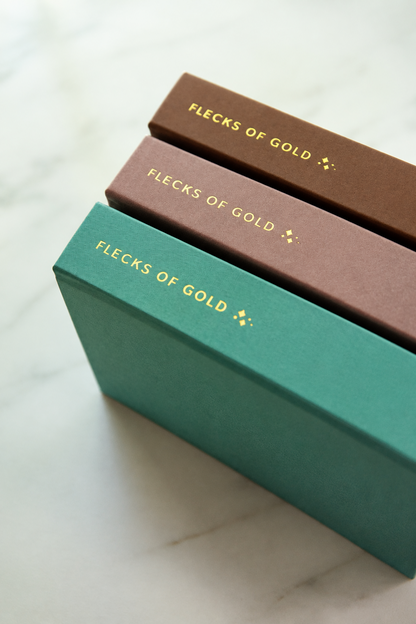 Angled view of camel, rose and teal Flecks of Gold journals stacked to show their gold-foil spines