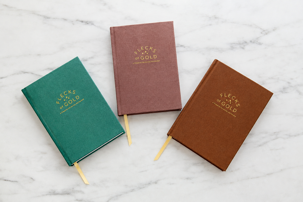 Three Flecks of Gold journals in teal linen, rose vegan leather and camel vegan leather laid flat on white marble