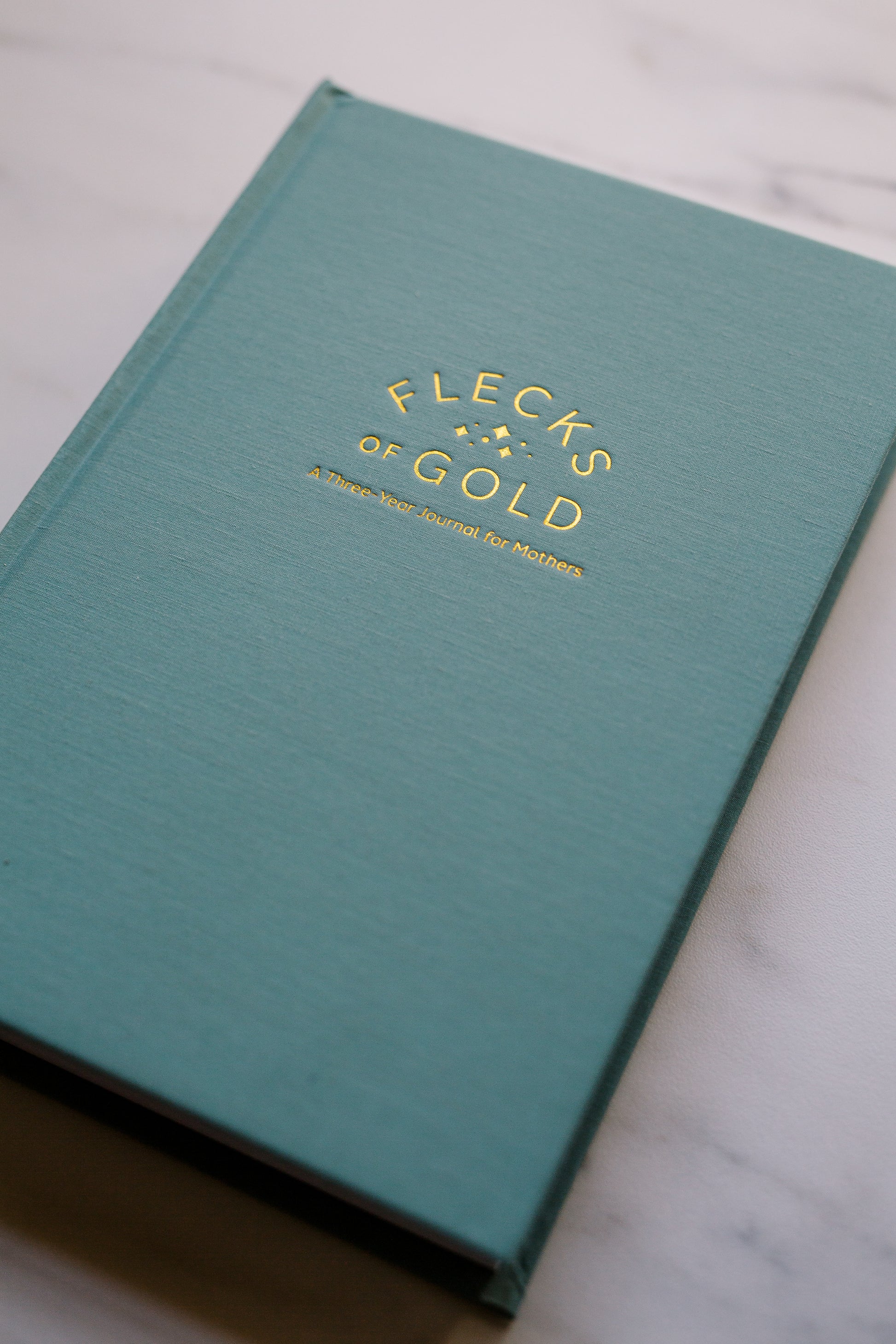 Beautiful Flecks of Gold Journal. Motherhood journal created by Rachel Nielson (host of the 3 in 30 Takeaways for Moms Podcast). A journal to help overwhelmed moms see the good, the magic, the gold in their everyday lives. Gold embossing.